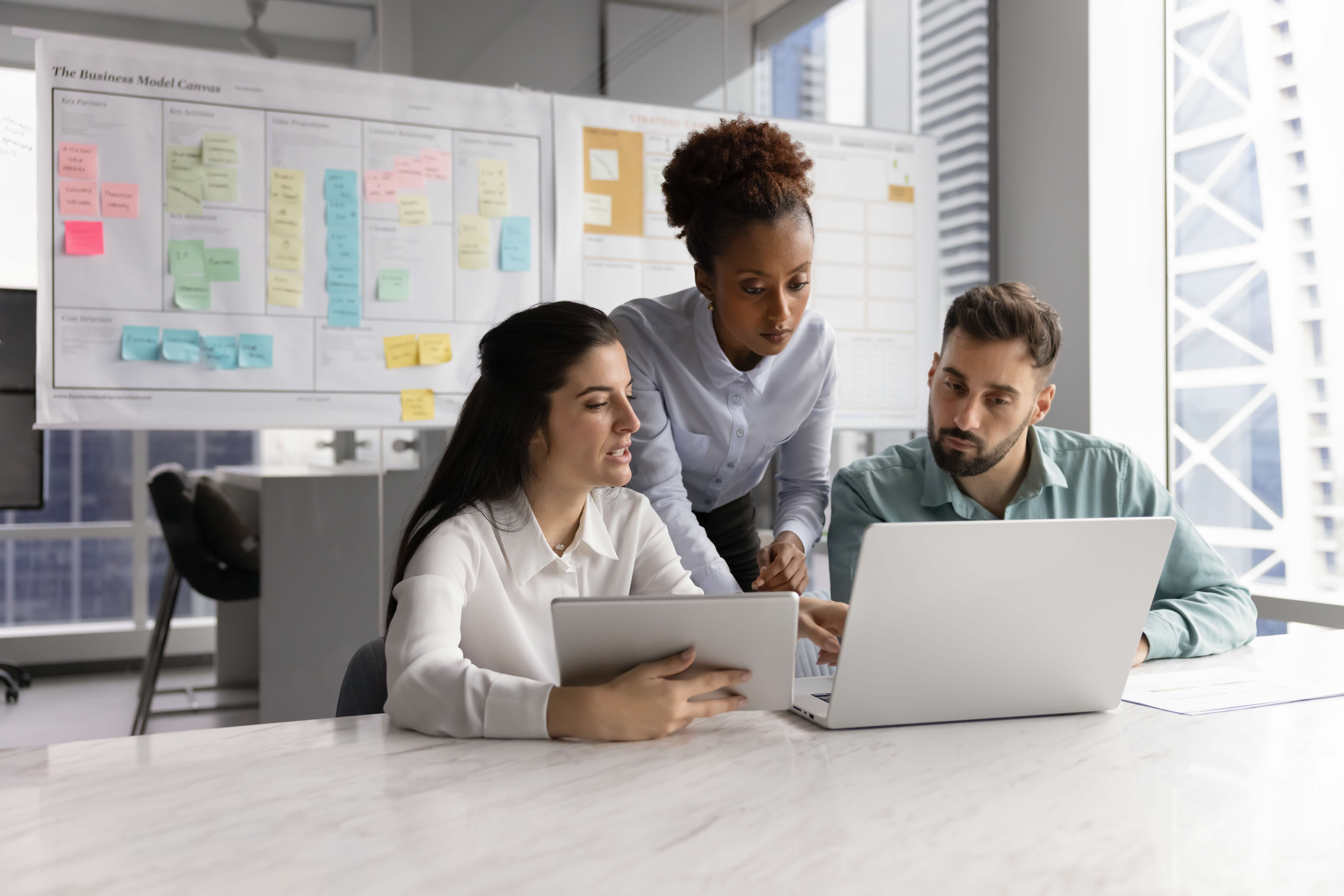 Three people working together, looking at a laptop and ipad